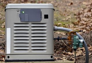Gray residential backup generator with gas line outdoors.