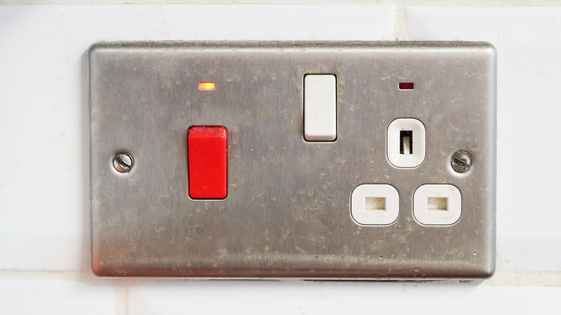 Metal UK electrical outlet with three switches, red and white, and two sockets.
