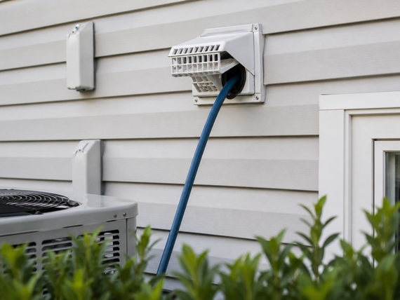 Blue hose connected to a wall vent on a beige house exterior, beside an outdoor AC unit