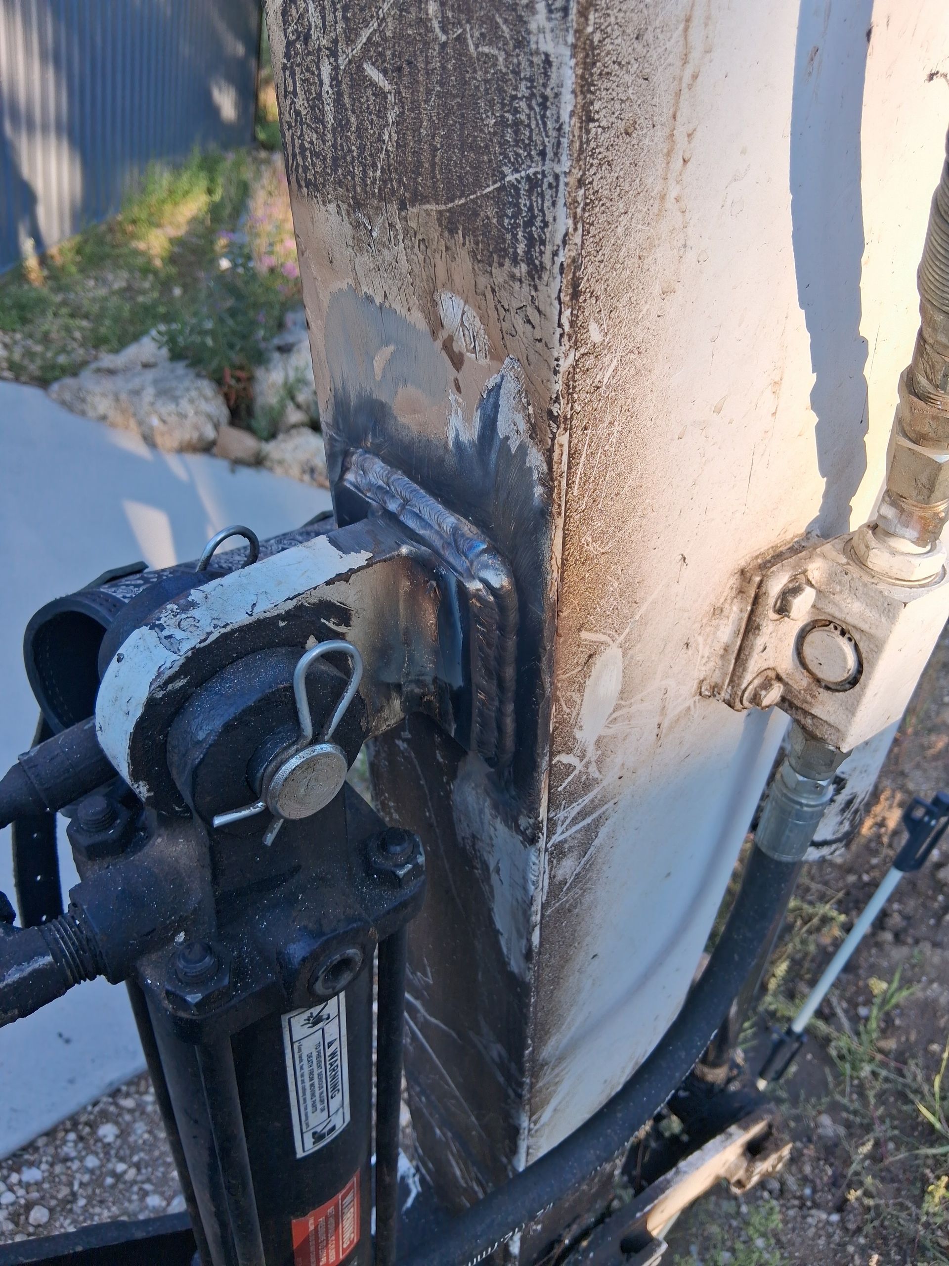 Close-up of a damaged black gate hinge and latch mounted on a weathered concrete post.
