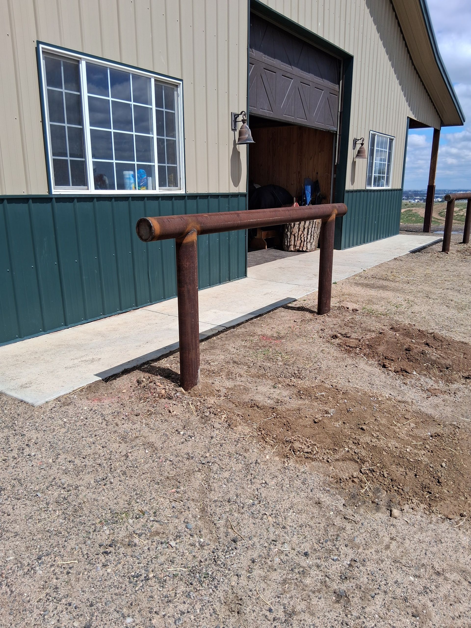 Rustic wooden handrail beside a barn entrance on a gravel path, with a window and open doorway.