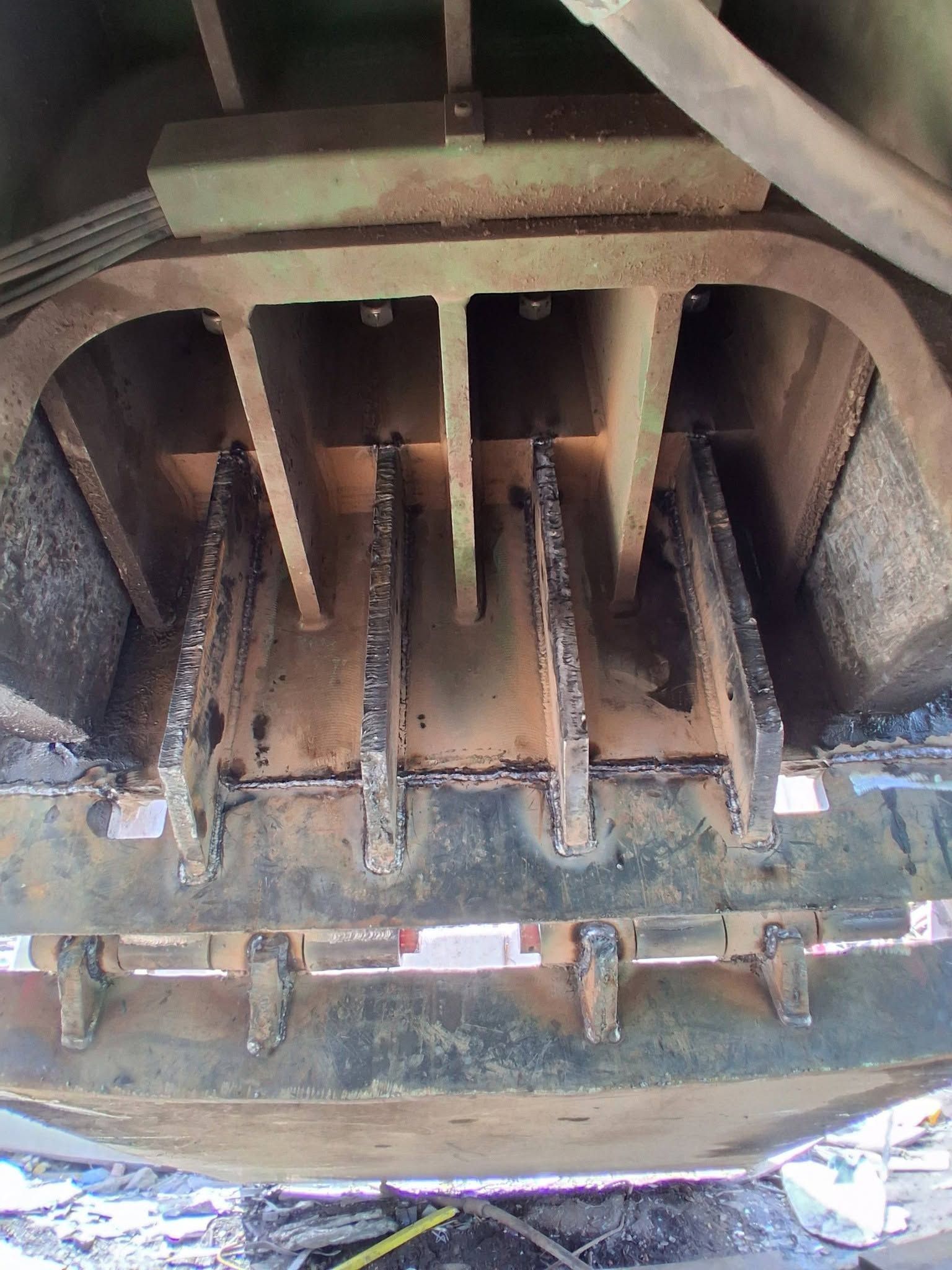 Steel I-beam assembly on sawhorses in a workshop, with welded plates and brackets.