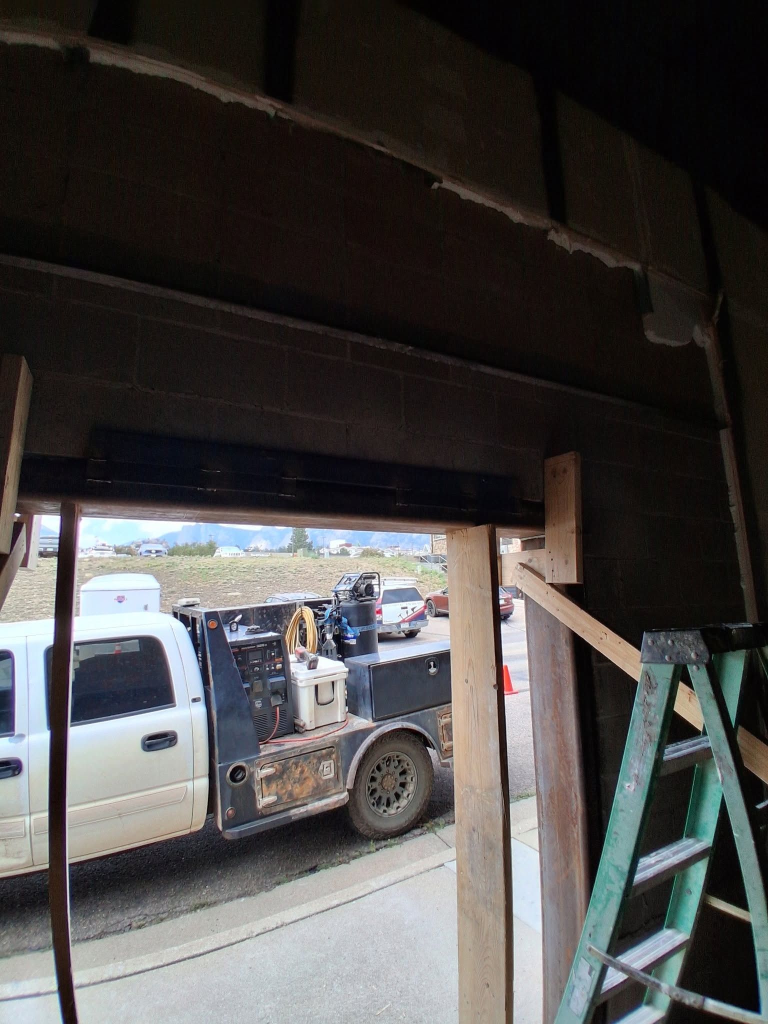 White utility truck parked beside a building, viewed through a dark doorway with a ladder on the right.