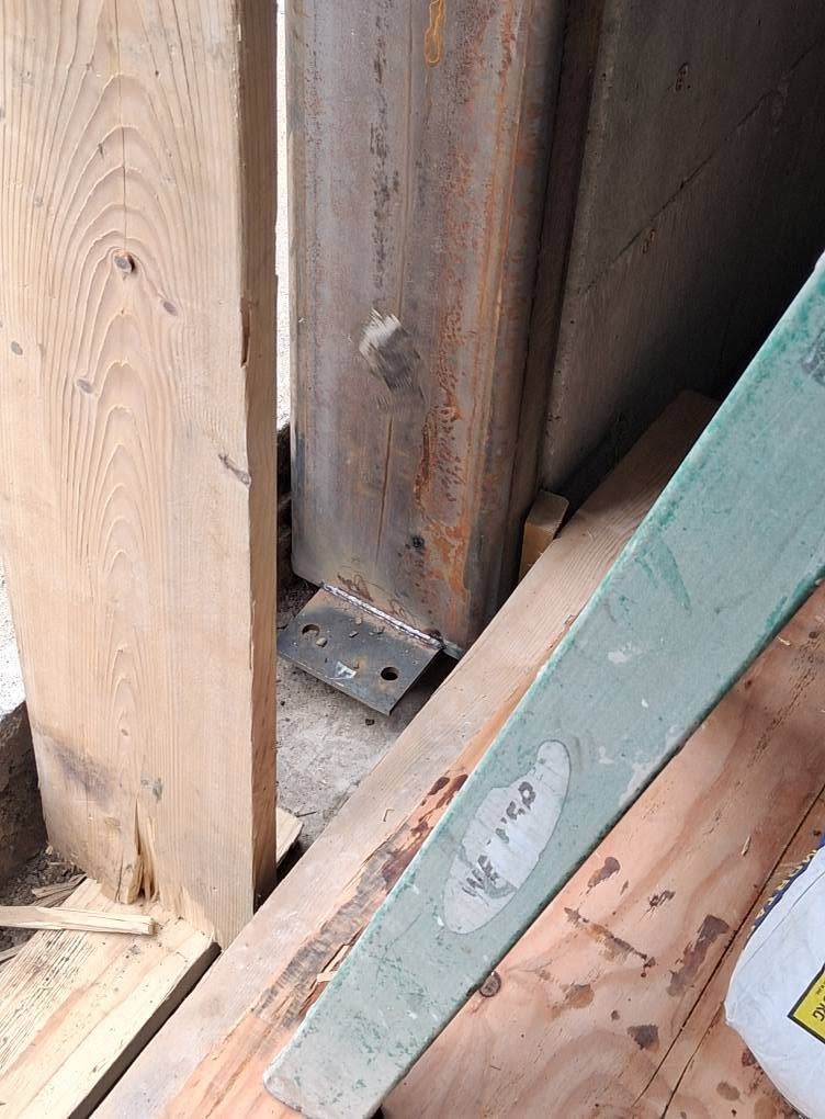 Close-up of wooden framing with a green board leaning against it and visible rusted metal hardware.