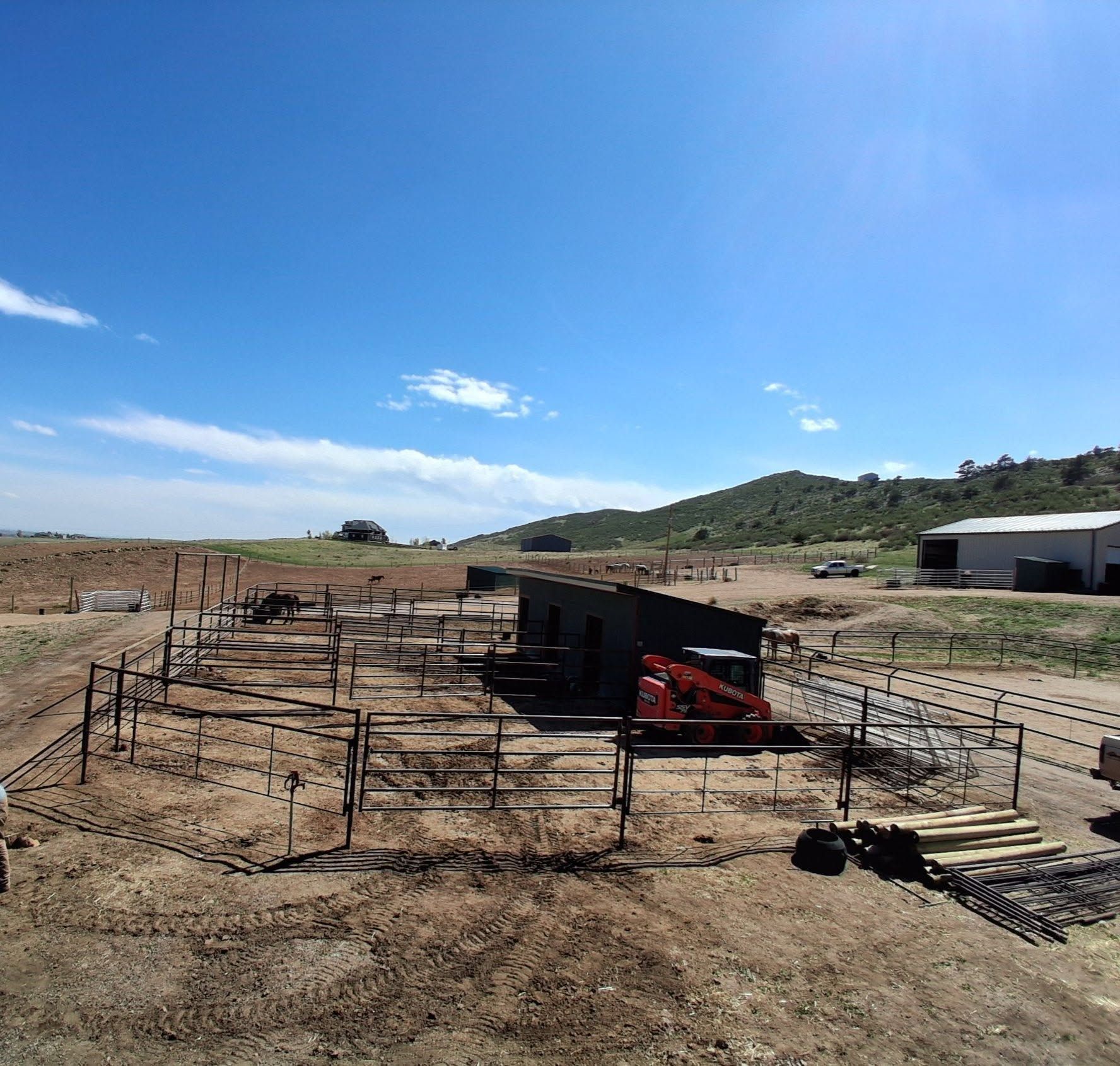 Open-air livestock pen on a dry farm under a bright blue sky, with hills in the background.