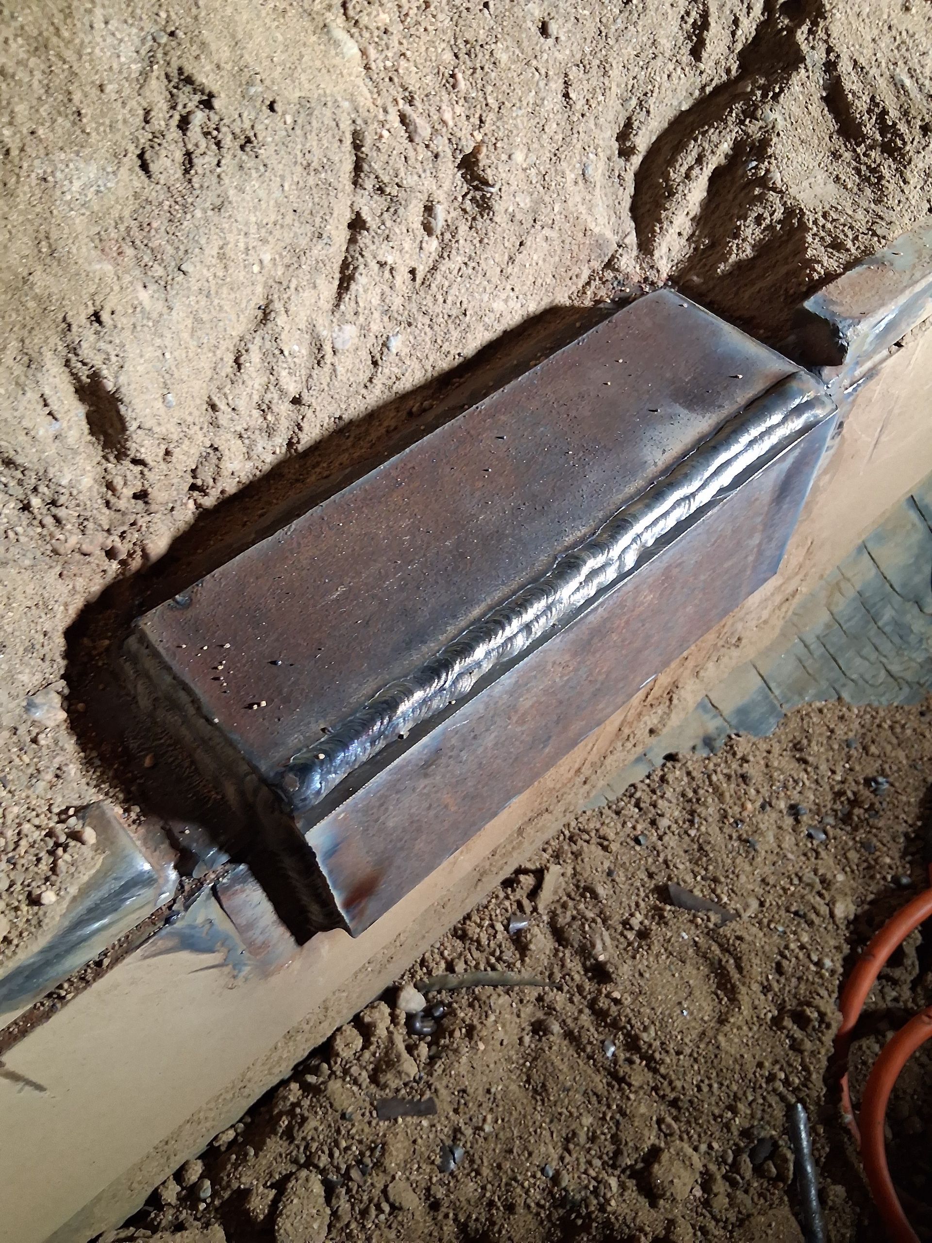 A metal rectangular object embedded in sand beside a pipe or cable.