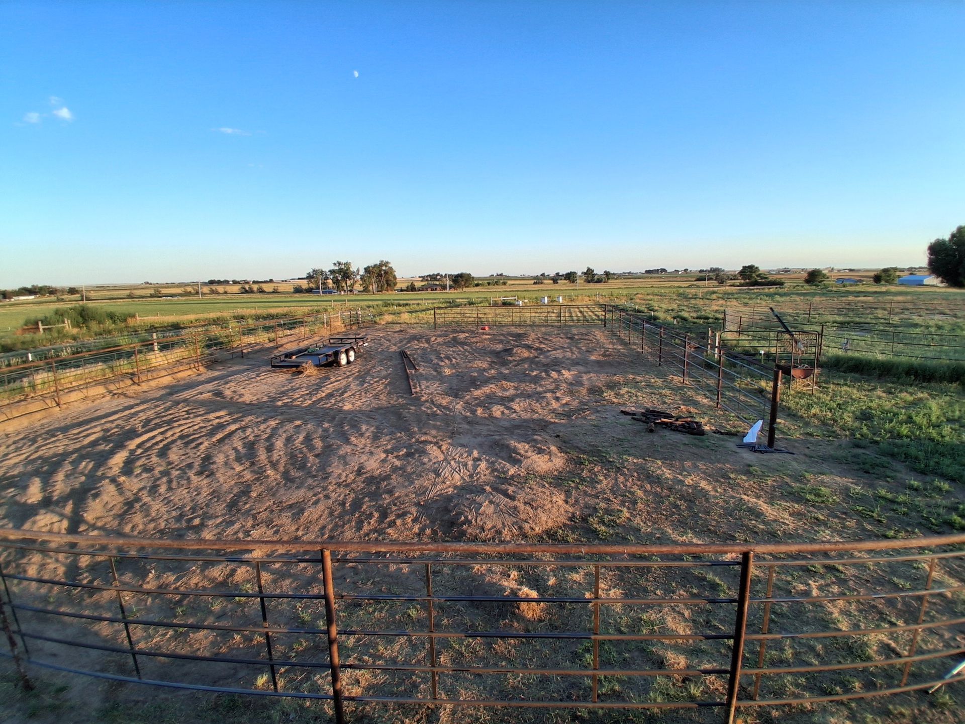 Fenced dirt paddock in open farmland at sunset, with a small figure in the distance and blue sky.