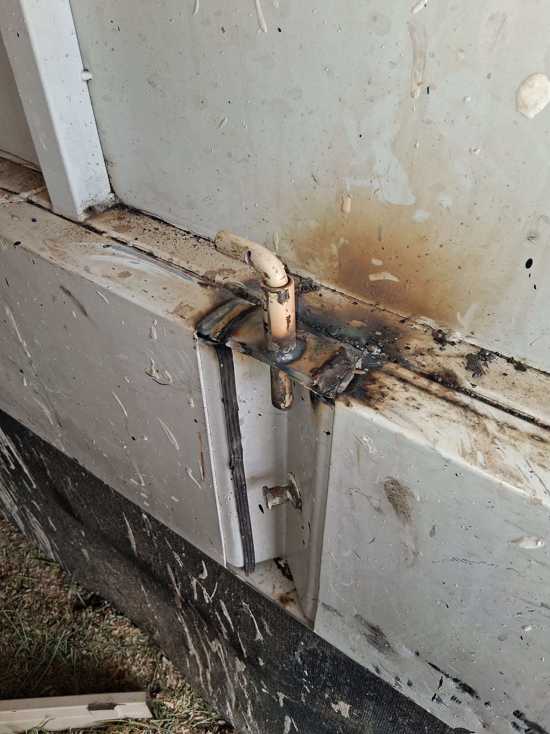 Rusty metal gate hinge with latch on a dirty white wall and concrete base