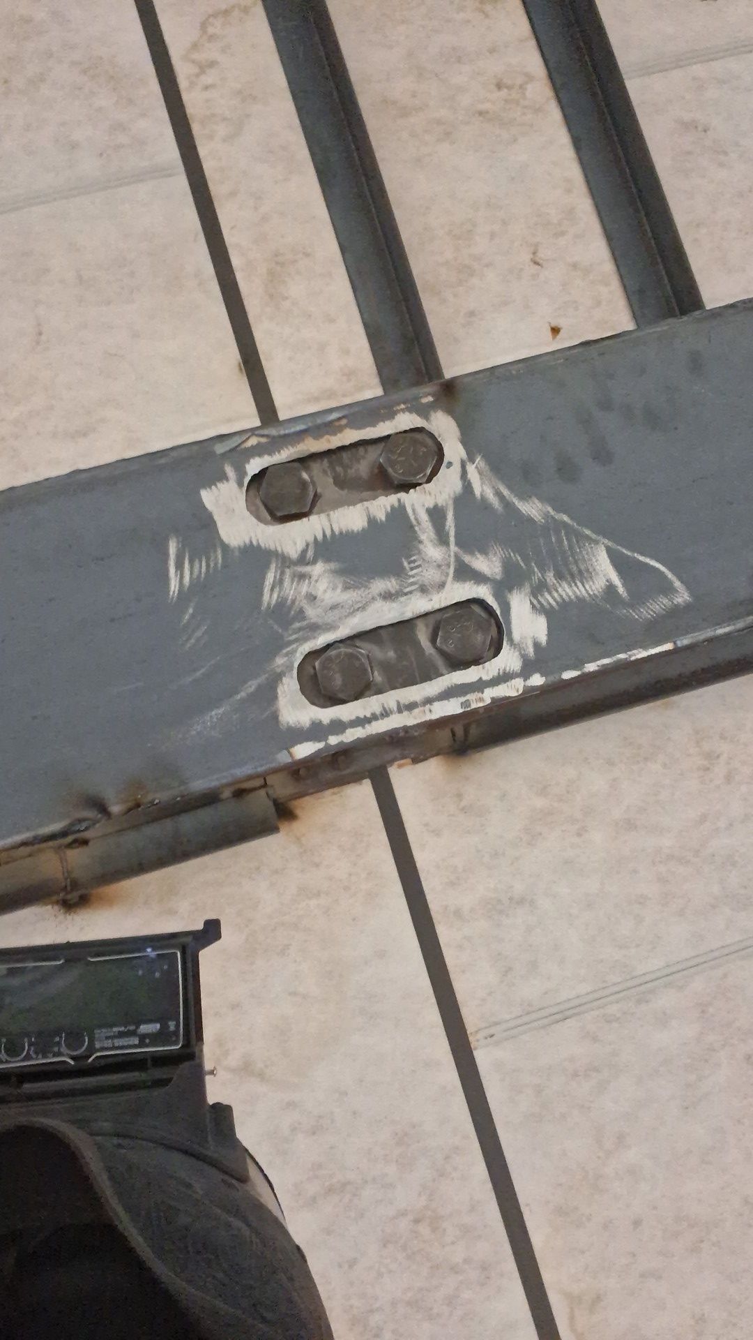 Close-up of a metal gate hinge bracket with welded repairs on beige tile flooring