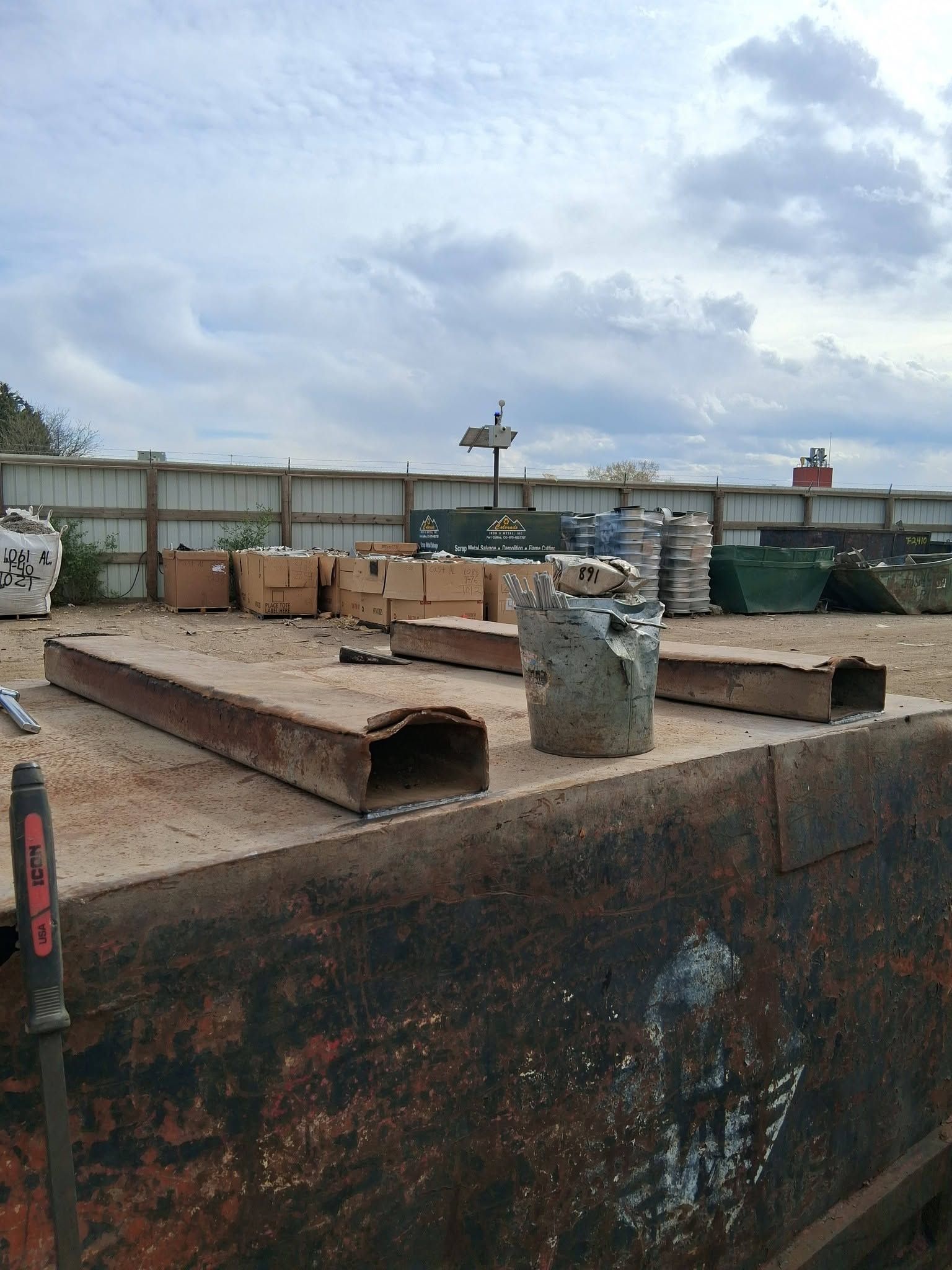 Rusty metal scraps on a large dumpster in an industrial yard under cloudy skies