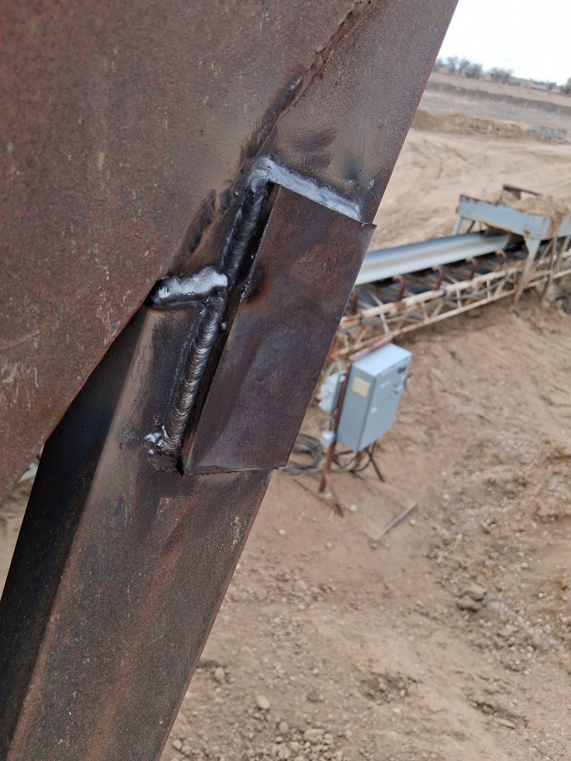 Close-up of a welded metal joint on a rusted beam at an outdoor industrial site.