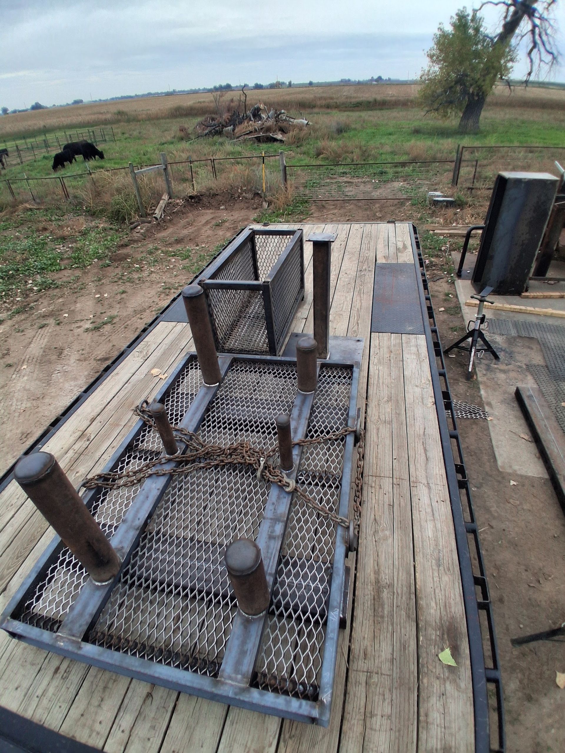 Outdoor farmyard scene with a rusty metal trap on a wooden pallet in a field