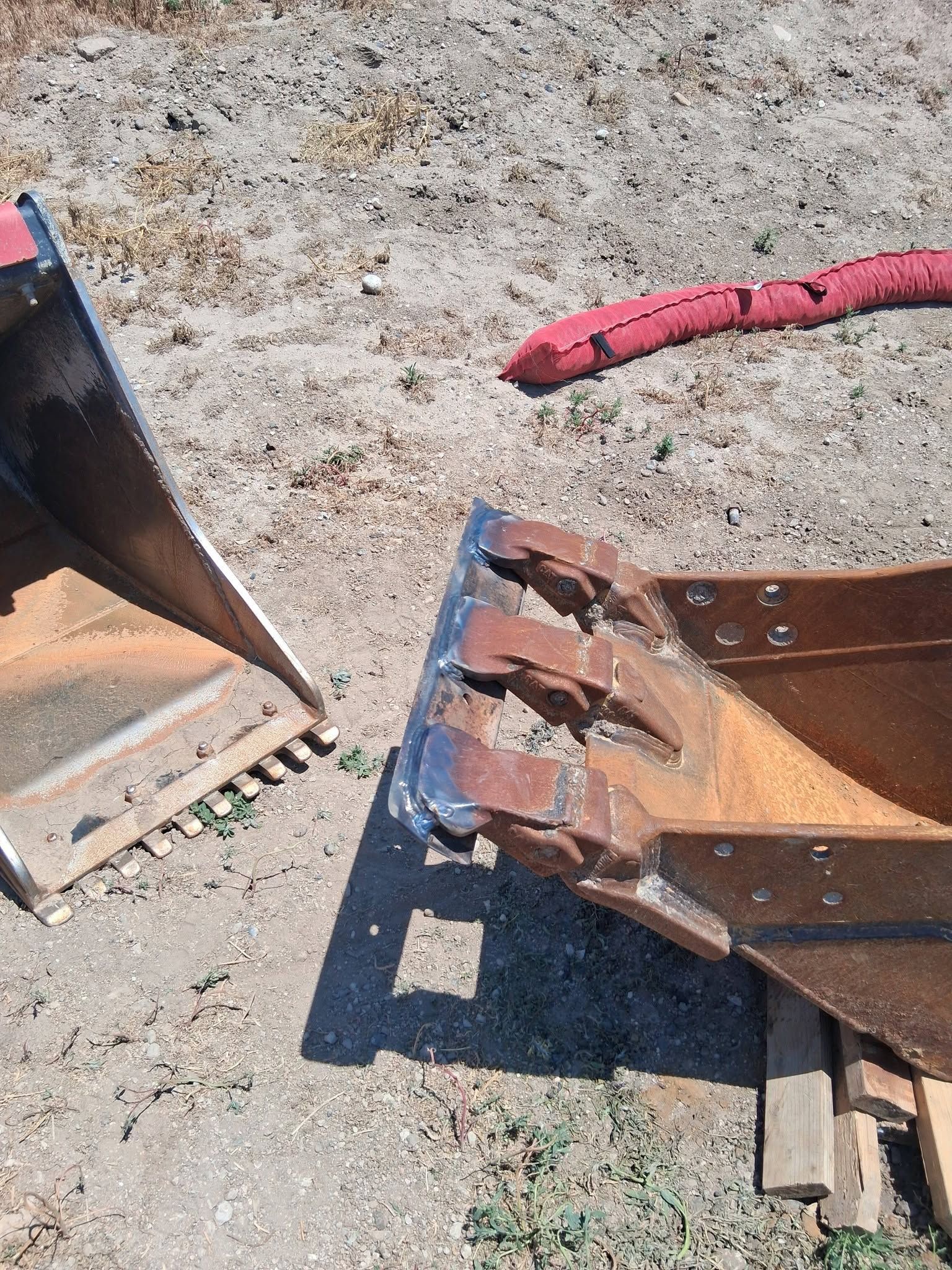 Two rusted metal machinery parts on gravel, one with a red hose attached.