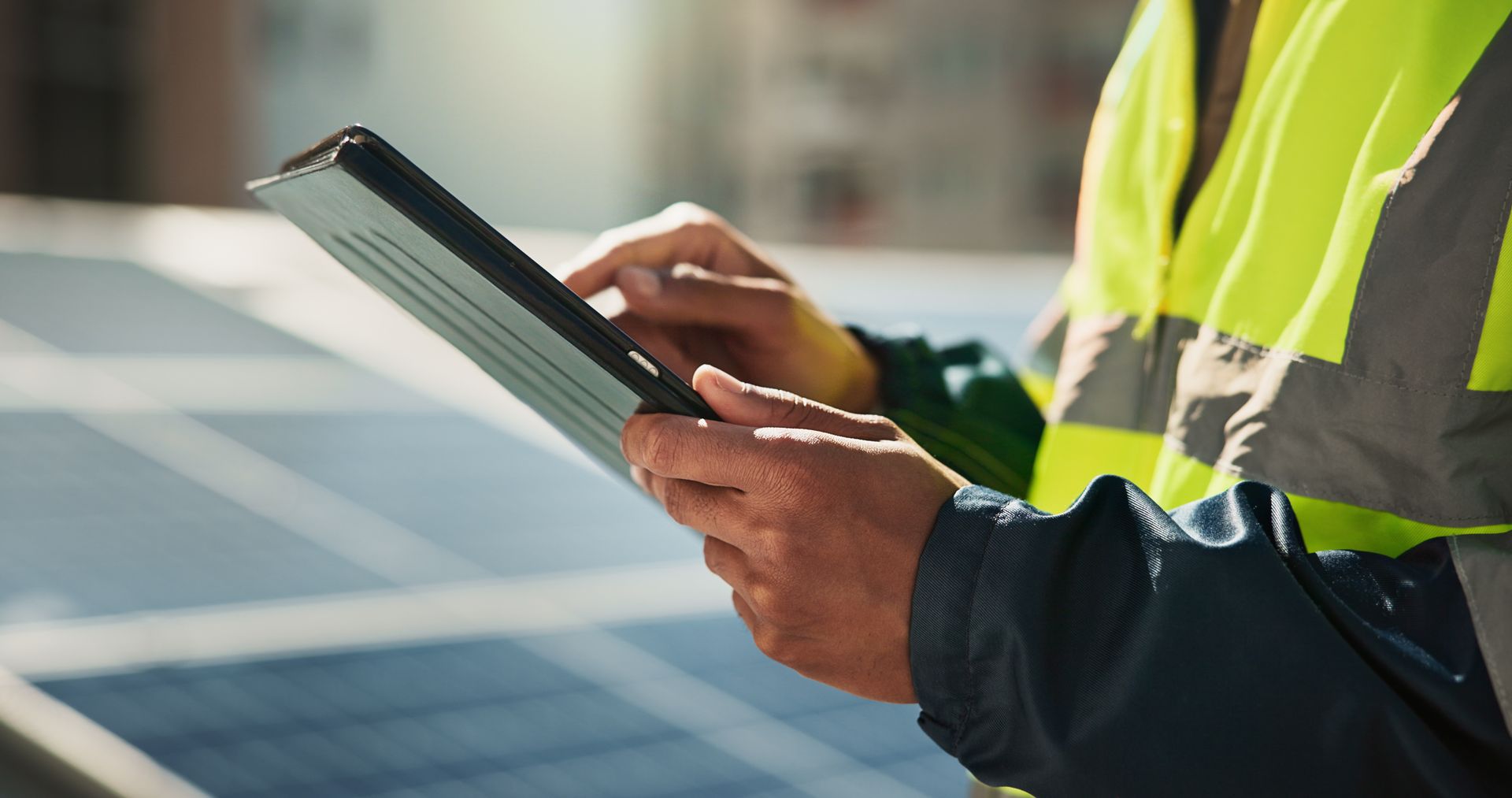 Un ouvrier portant un gilet haute visibilité utilise une tablette tout en inspectant des panneaux solaires.