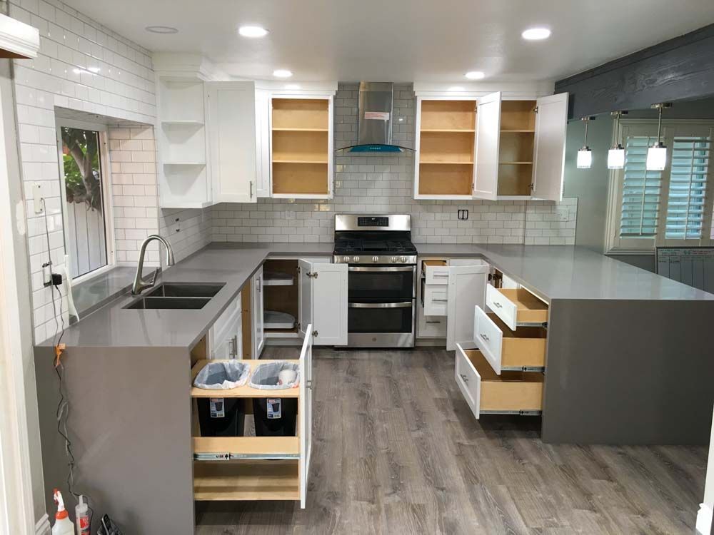 A brand new, remodeled, kitchen with a stove, sink, and drawers open.