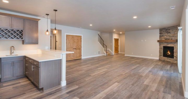 A kitchen and living room in an empty house with hardwood floors and a fireplace.