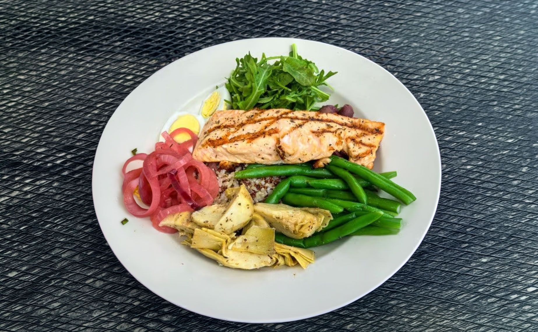 Grilled salmon with green beans, potatoes, and pickled onions on a white plate