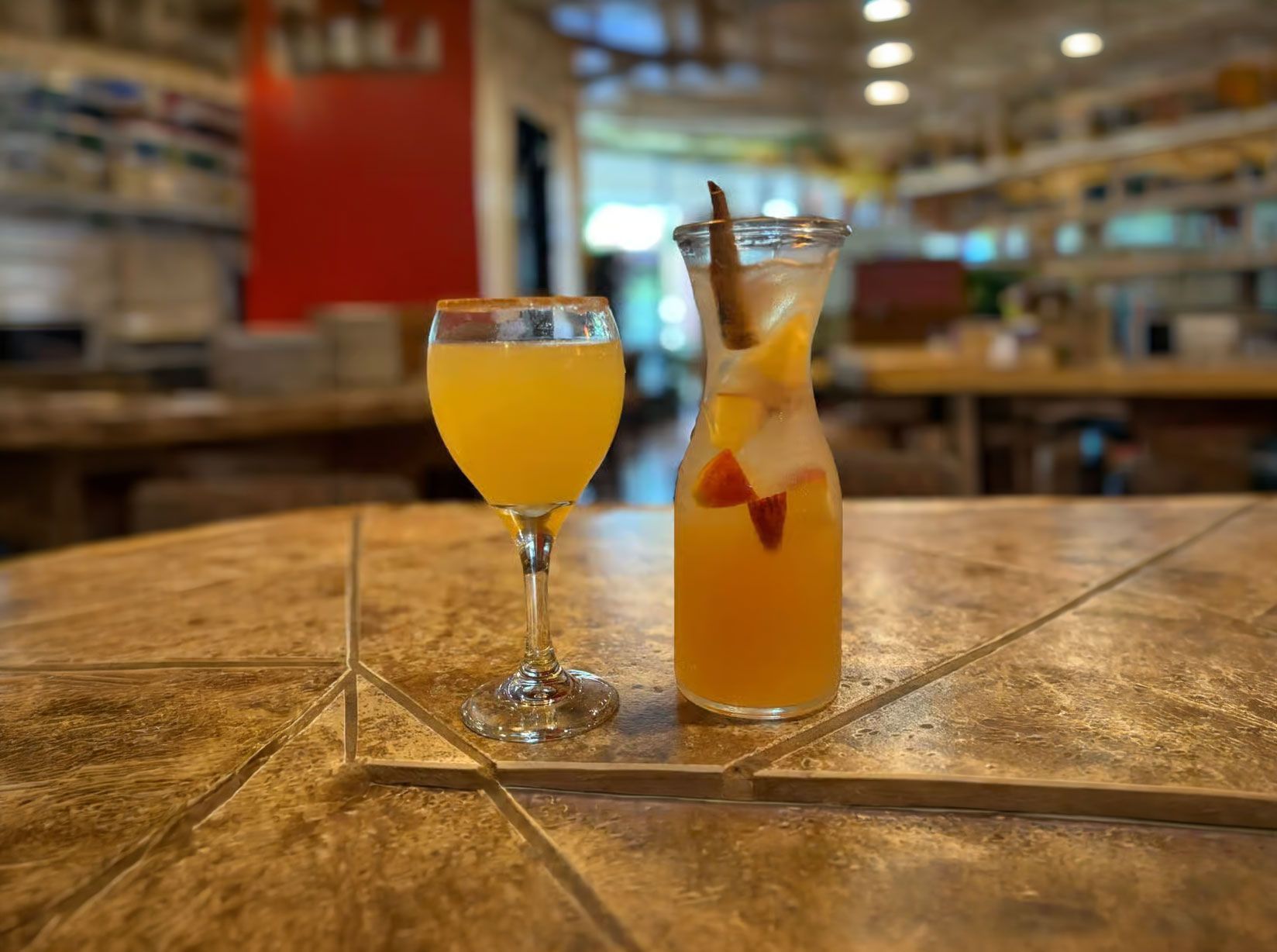 Two orange cocktails on a wooden bar in a softly lit restaurant.