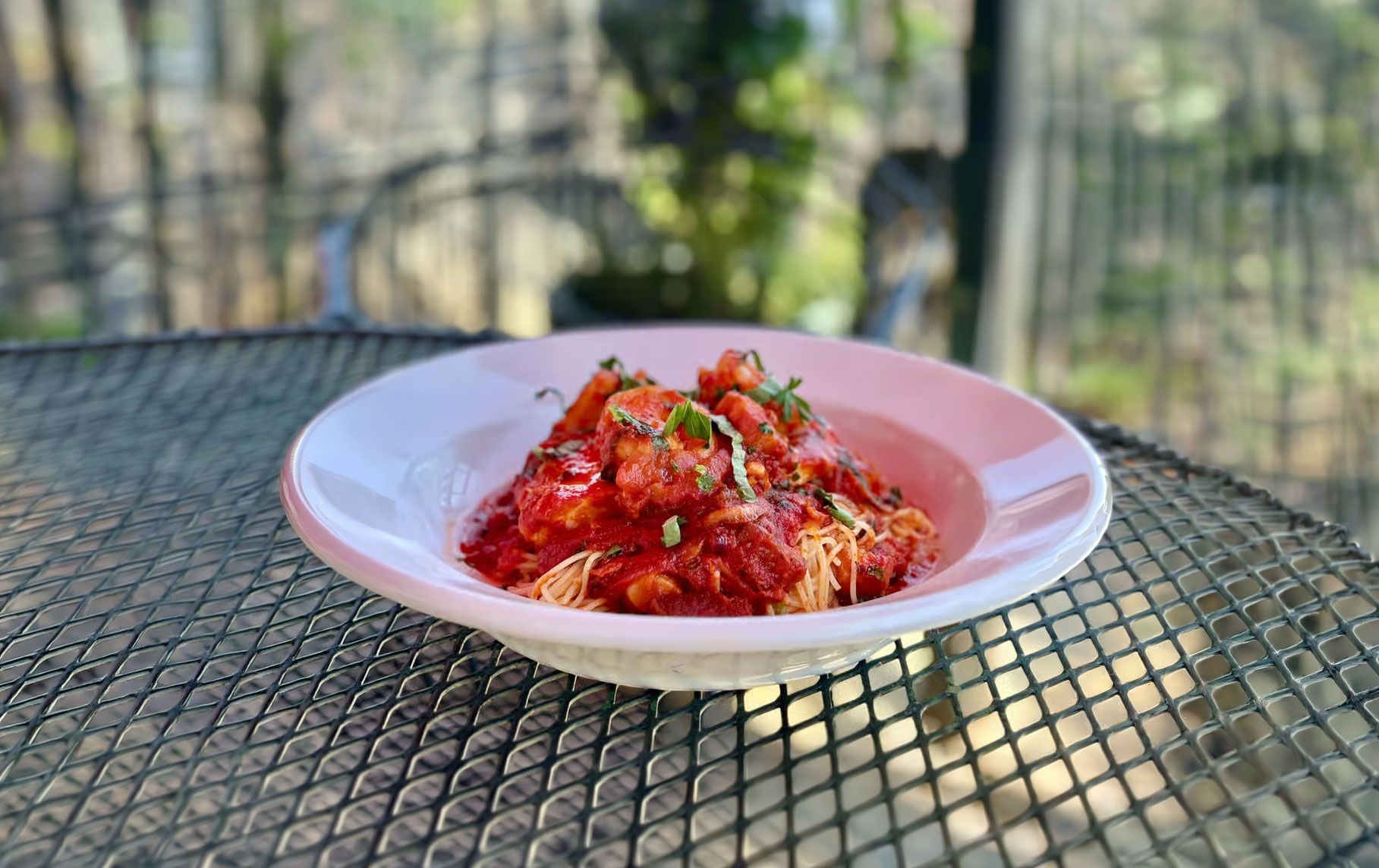 Plate of red sauced pasta topped with herbs on a table outdoors.