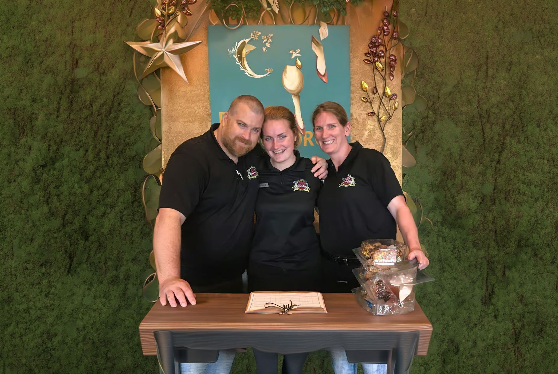 Three smiling staff members in black shirts pose behind a table at a rustic event booth.