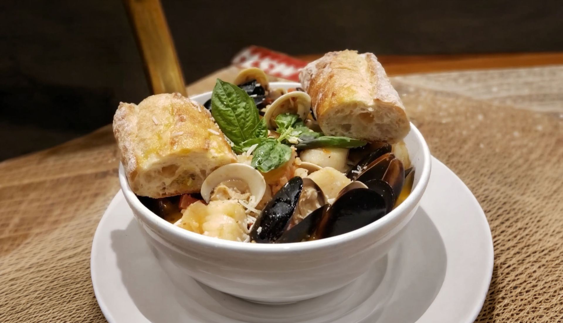 Bowl of noodle soup with shrimp, mussels, and vegetables on a white plate.