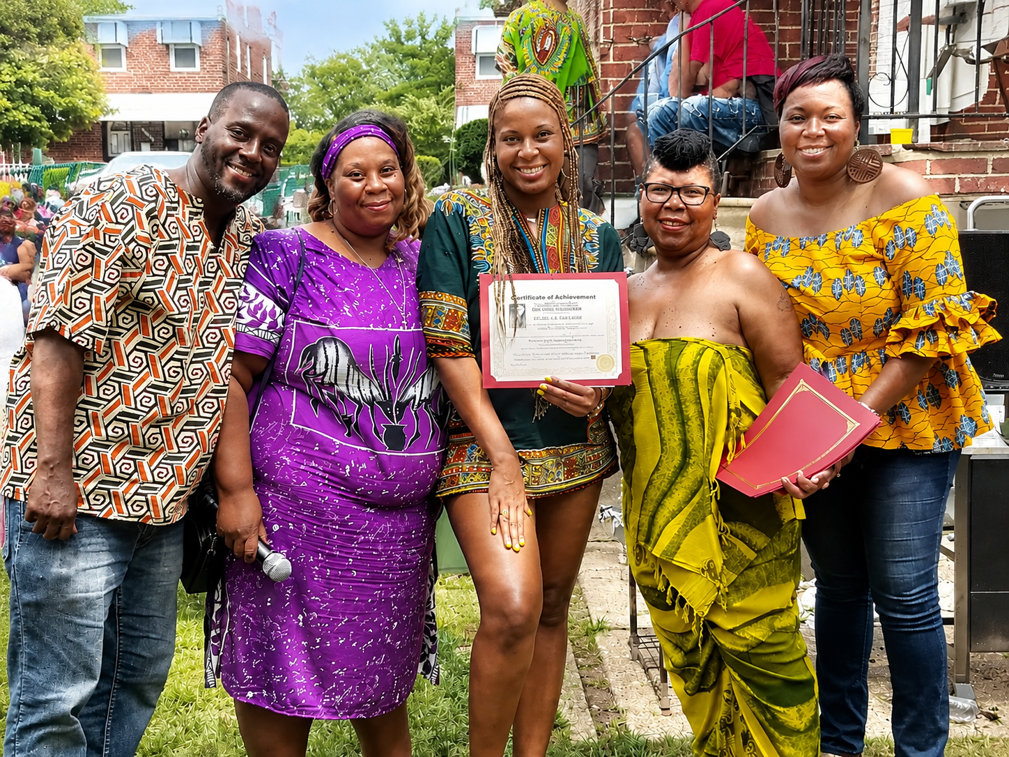 Five people posing outdoors, one holding a certificate and another holding a pink folder.