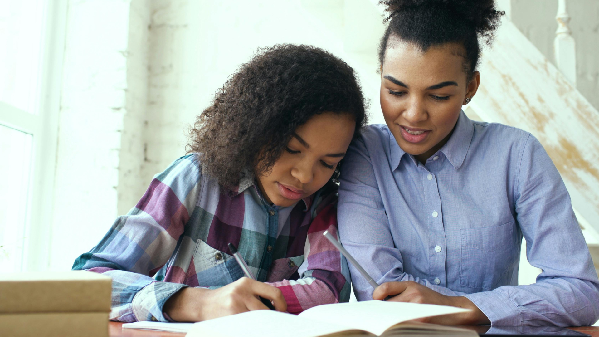 Two people reading a book together on a couch, smiling and leaning over the pages.