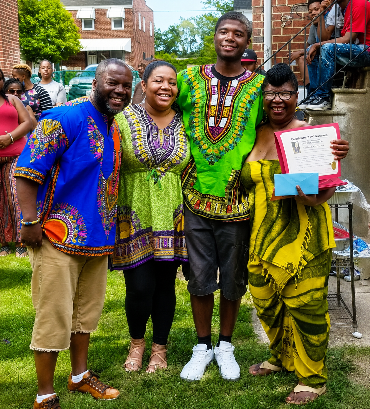 Four people in colorful patterned outfits smiling outdoors, posing together on steps.