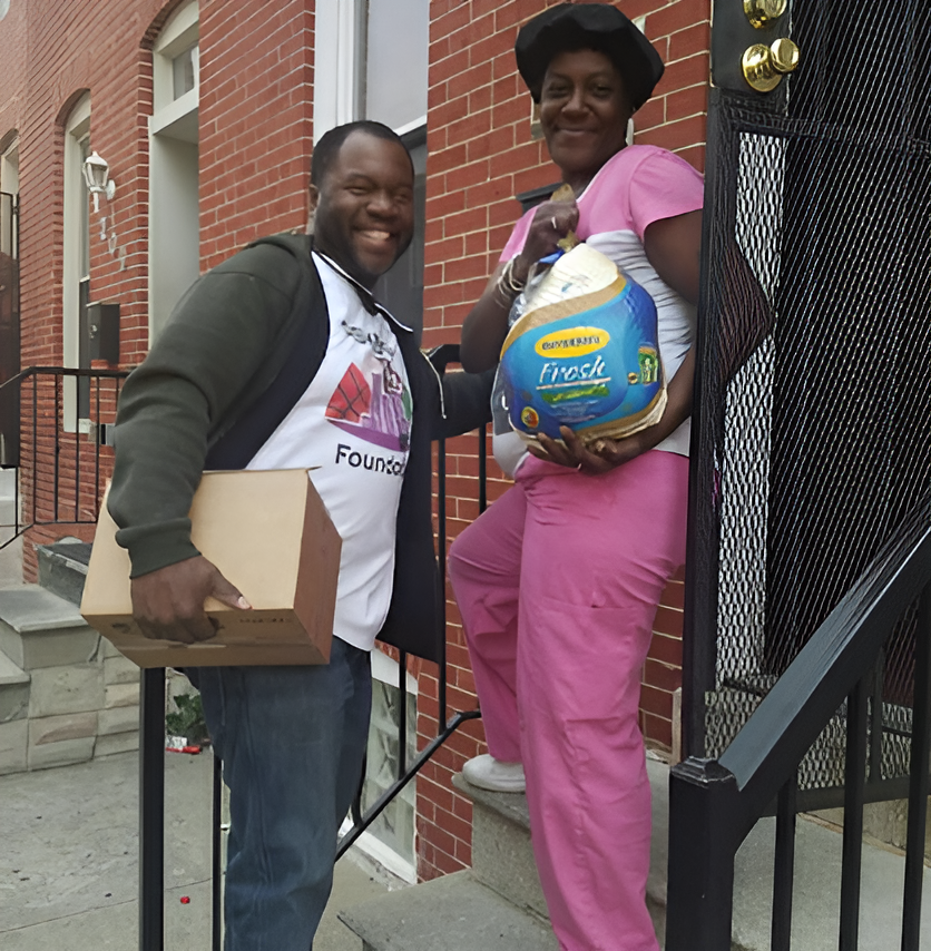Two people on a porch, smiling and holding boxes and a large pack of paper towels.