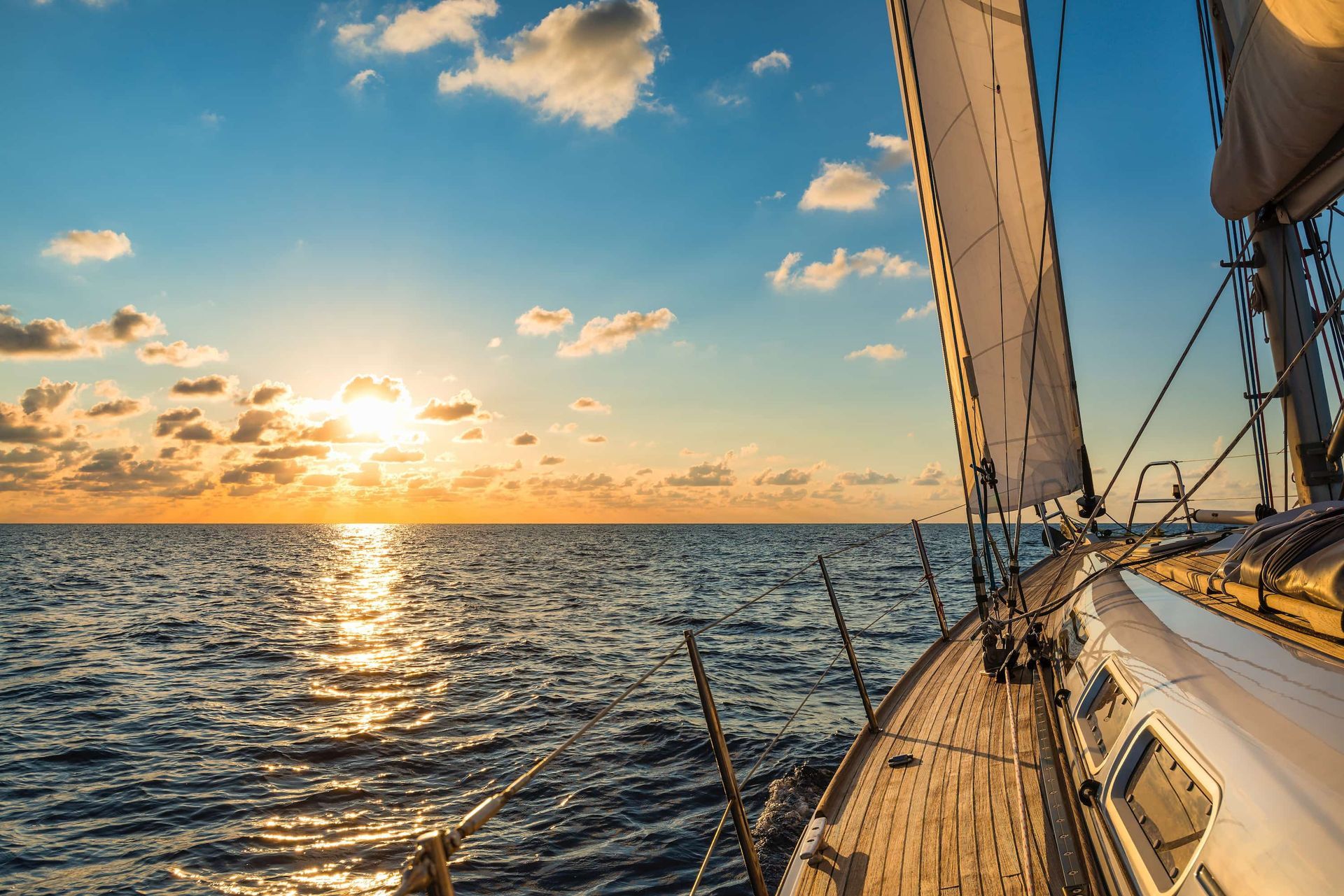 Sailboat on ocean at sunset; golden sky, open sail, wooden deck.