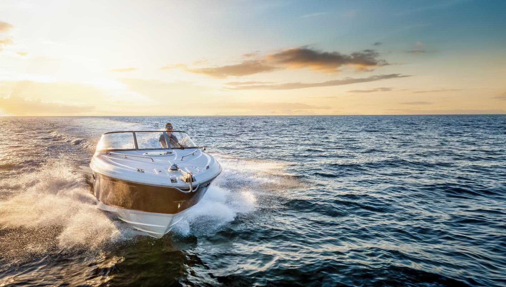 Boat speeding across ocean at sunset, creating white water.