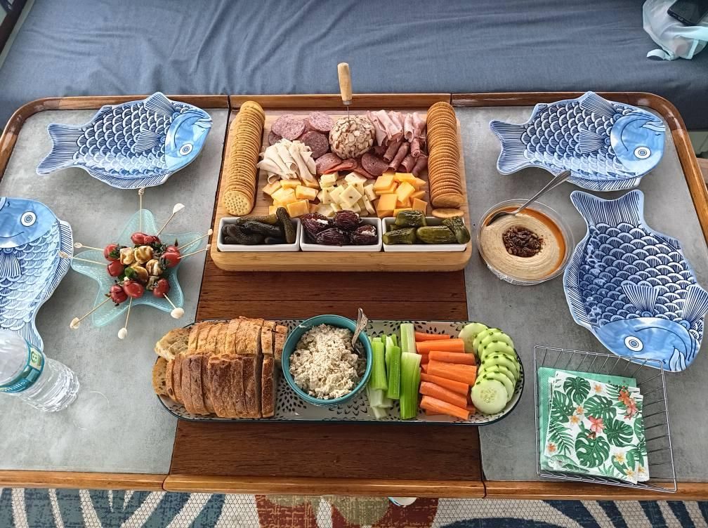 Charcuterie board with meats, cheeses, crackers, dips, vegetables, and bread served on a table with fish-shaped plates.