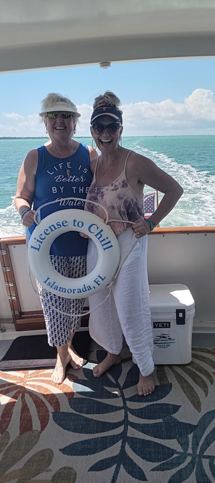 Two women on a boat holding a life preserver that says 