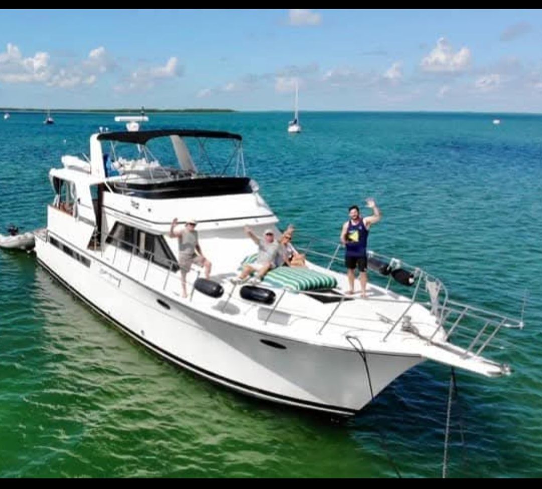 People waving from a white motor yacht in turquoise water. Clear blue sky, sunny day.
