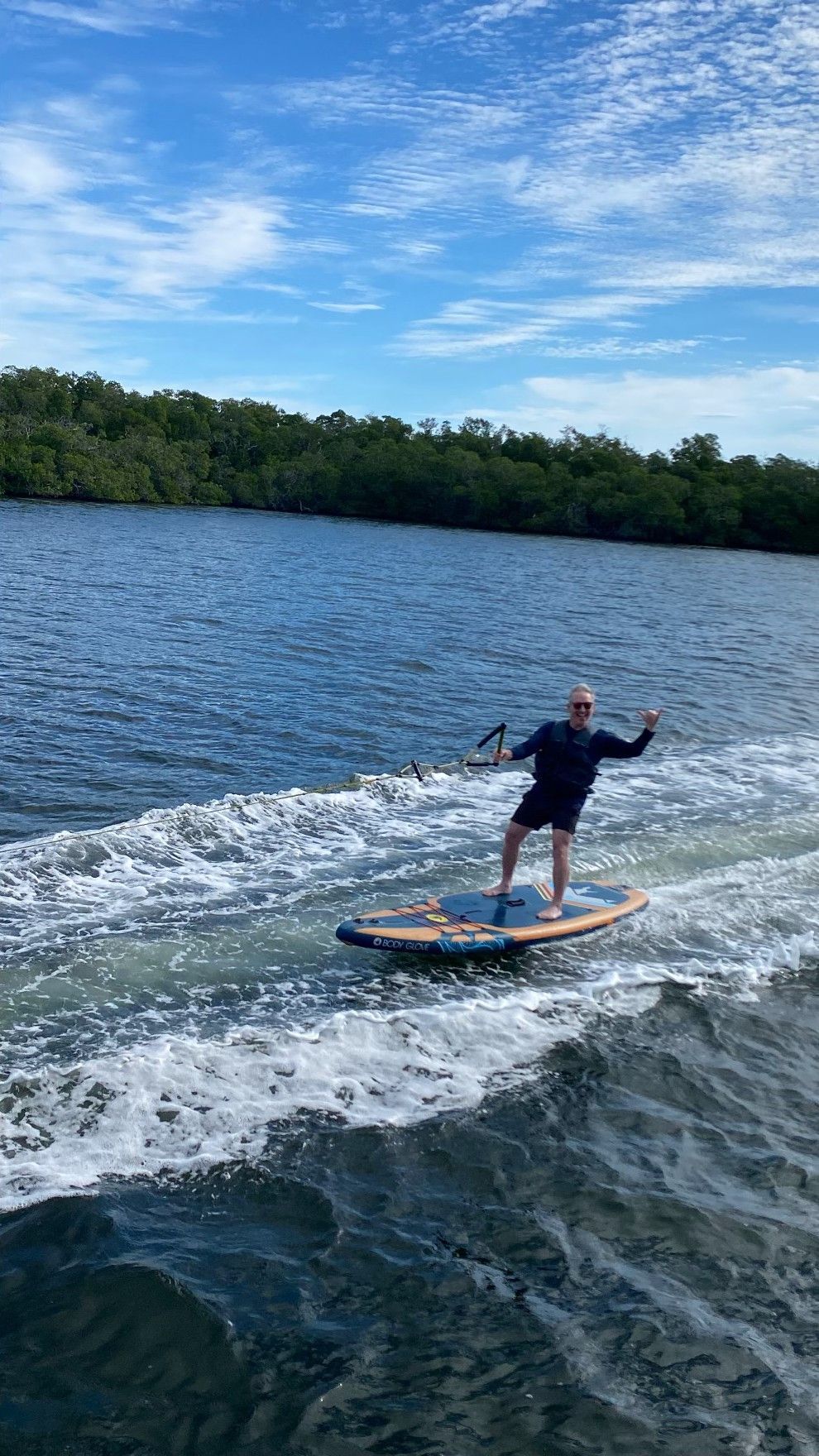 Man on motorized surfboard in blue water, arms outstretched, under a blue sky.