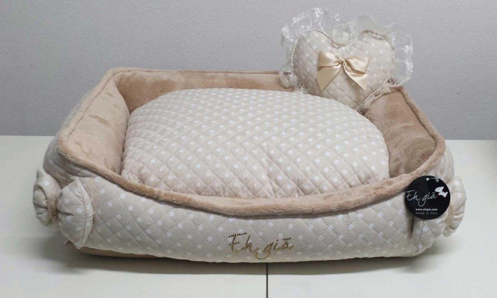 Cuccia beige per animali con cuscino a pois bianchi e un fiocco decorativo, su una superficie bianca
