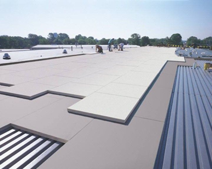 Workers installing insulation panels on a large commercial roof. Gray and white colors. Blue sky.