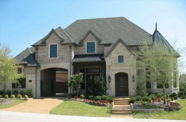 Brick and stone house with a dark roof and landscaping. Driveway leads to a covered entryway.