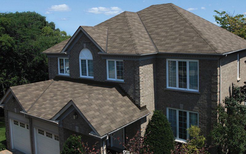 Two-story brick house with a brown roof and white-framed windows on a sunny day.