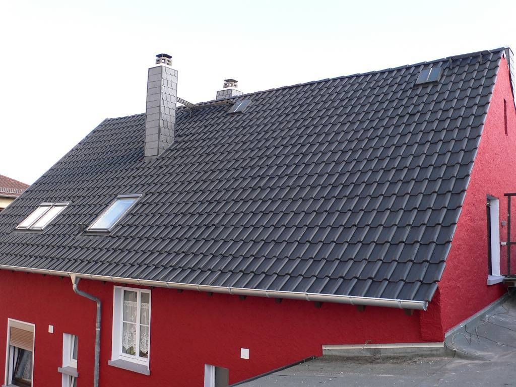 Red building with dark gray tiled roof, chimneys, and skylights.