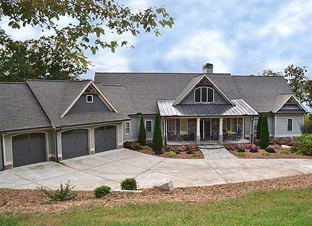 Gray house with three-car garage, front porch, and driveway on a grassy hill under a cloudy sky.