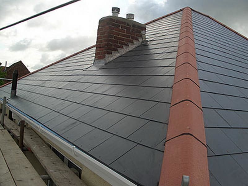 Newly installed dark gray slate roof with brick chimney and red trim.