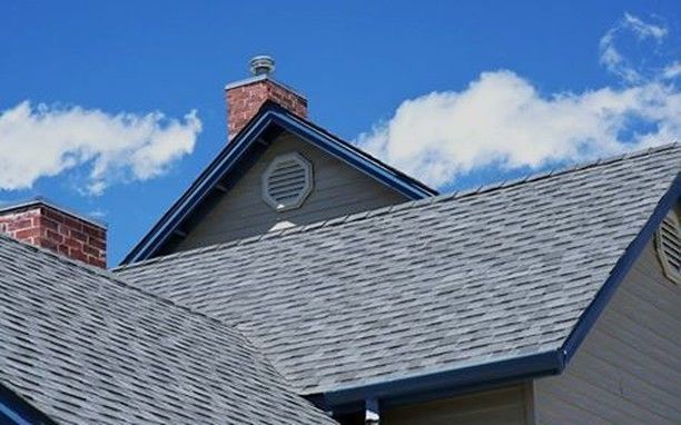 Gray asphalt shingle roof on a house with a brick chimney and blue sky.