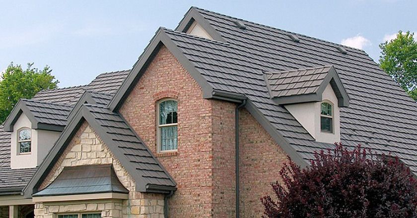 Brick house with gray tiled roof, dormers, and stone accents against a blue sky.