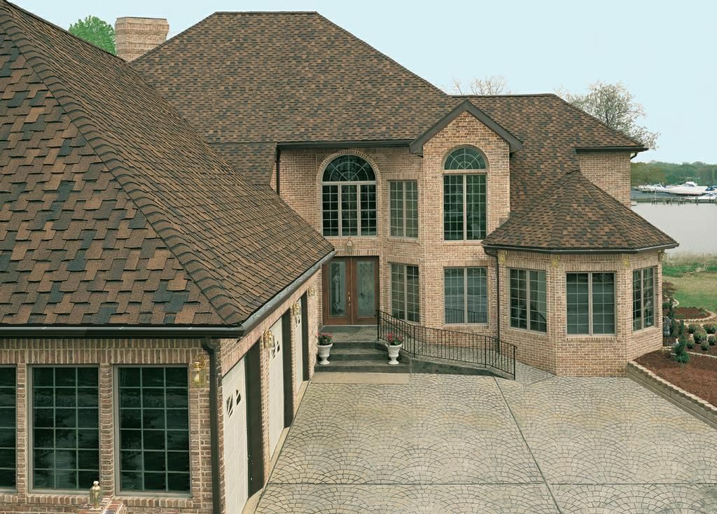Two-story brick house with brown roof and attached garage, overlooking water.
