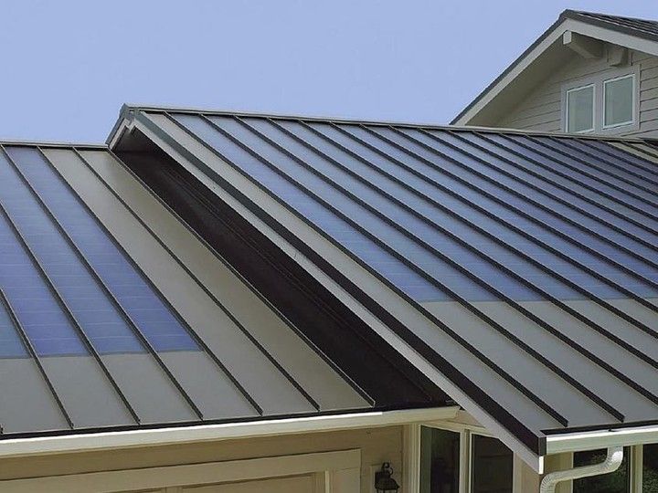 Dark metal roof with integrated solar panels on a house, with a blue sky background.