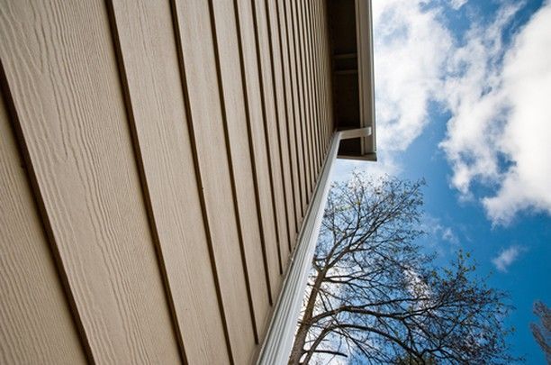 Beige siding and gutter on a house against a blue sky, tree in the background.