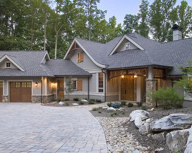 Gray house with a stone driveway, garage, and front entrance, nestled among trees.