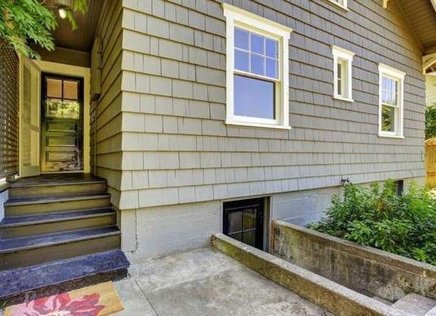 Exterior of a house with gray siding, front steps, and a basement entrance.