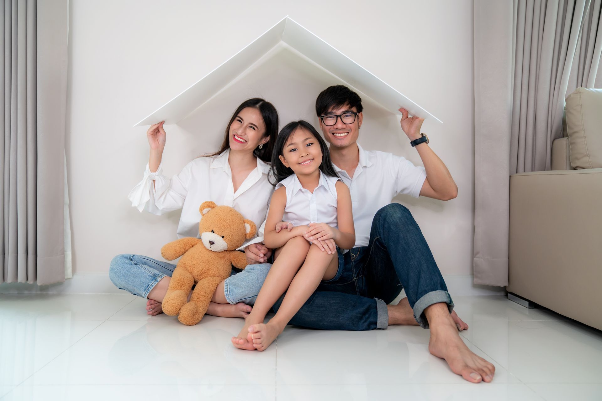 A family is sitting on the floor under a cardboard house.